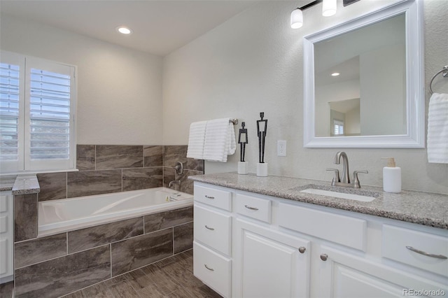 bathroom with vanity, hardwood / wood-style floors, and tiled tub