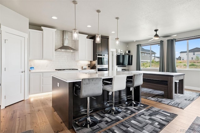 23814 E 36th Pl, Aurora, CO 80019 - kitchen with wall chimney exhaust hood, light wood finished floors, a kitchen island, stovetop, and light countertops
