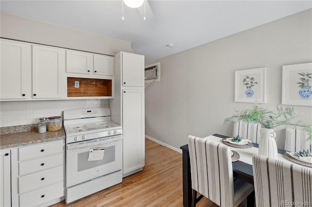 kitchen with backsplash, white gas range oven, light wood-style floors, white cabinets, and baseboards