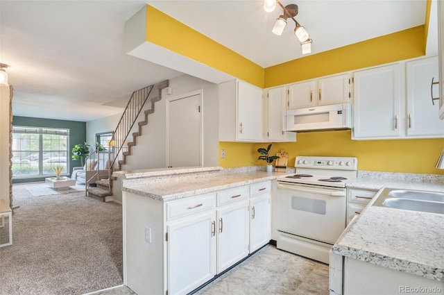 kitchen with a peninsula, white appliances, a sink, and white cabinets