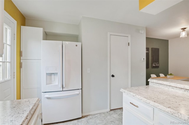 kitchen featuring white fridge with ice dispenser, white cabinets, baseboards, and light stone countertops