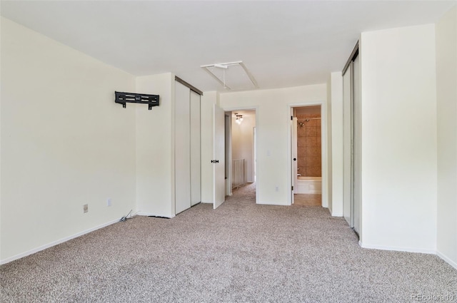 unfurnished bedroom featuring ensuite bathroom, light carpet, baseboards, two closets, and attic access