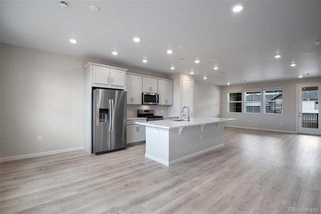 kitchen featuring a kitchen island with sink, white cabinets, sink, light wood-type flooring, and stainless steel appliances