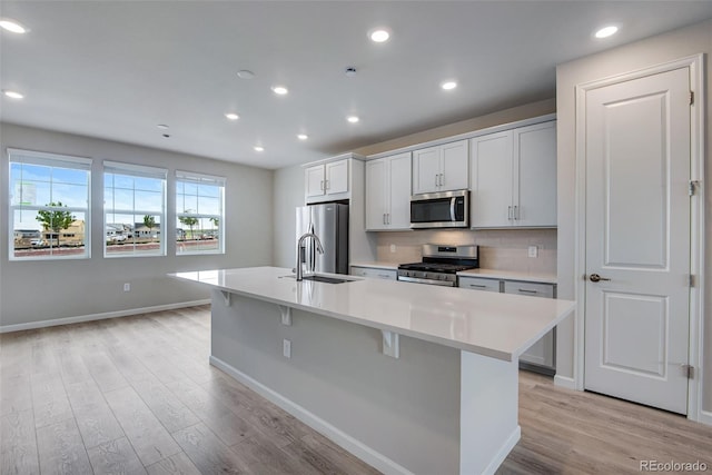 kitchen featuring sink, light wood-type flooring, a kitchen island with sink, and appliances with stainless steel finishes