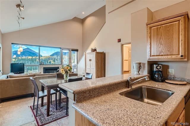 kitchen featuring light stone counters, kitchen peninsula, sink, and high vaulted ceiling