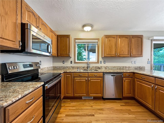 642 52nd Ave, Greeley, CO 80634 - kitchen with appliances with stainless steel finishes, light wood-type flooring, brown cabinets, a textured ceiling, and light stone countertops