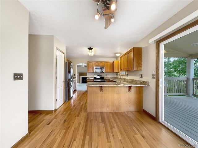 642 52nd Ave, Greeley, CO 80634 - kitchen featuring stainless steel appliances, a peninsula, brown cabinetry, and light wood-style flooring