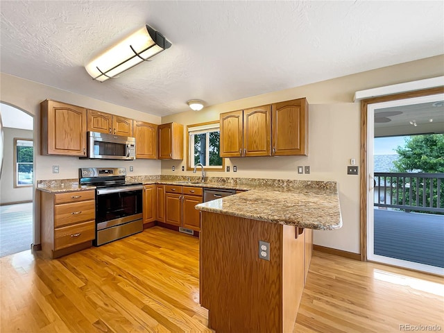 642 52nd Ave, Greeley, CO 80634 - kitchen with appliances with stainless steel finishes, a peninsula, light wood-style floors, brown cabinets, and a textured ceiling