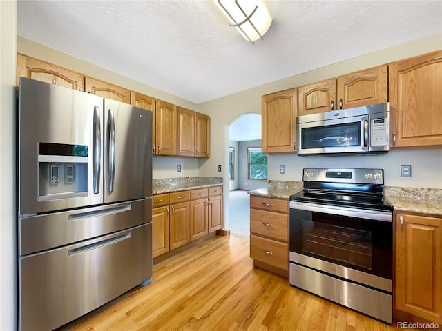 642 52nd Ave, Greeley, CO 80634 - kitchen featuring stainless steel appliances, light wood-style flooring, arched walkways, and light stone countertops