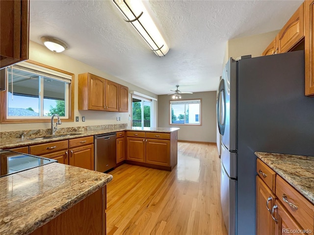 642 52nd Ave, Greeley, CO 80634 - kitchen featuring stainless steel appliances, a peninsula, light wood finished floors, a textured ceiling, and brown cabinetry