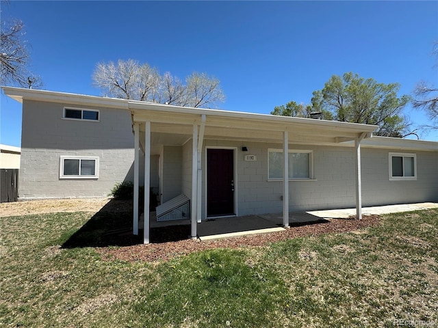 rear view of house with a lawn and concrete block siding