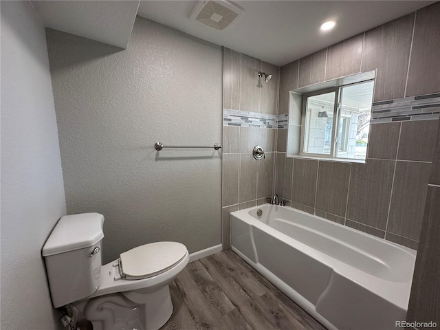 full bath featuring toilet, wood finished floors, washtub / shower combination, visible vents, and baseboards