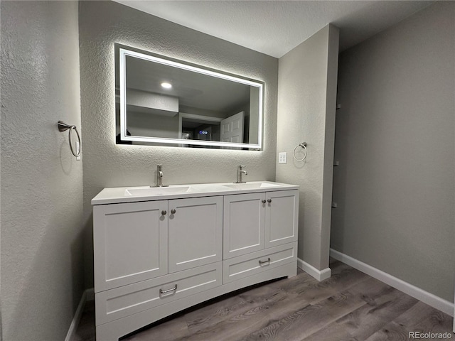 full bathroom with a textured wall, wood finished floors, and a sink
