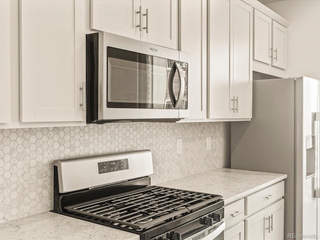 kitchen with white cabinetry, backsplash, light stone counters, and appliances with stainless steel finishes