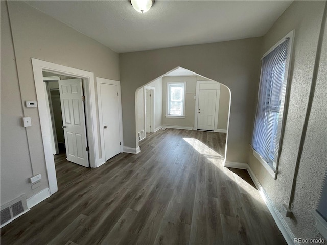 interior space with baseboards, visible vents, arched walkways, and dark wood-type flooring