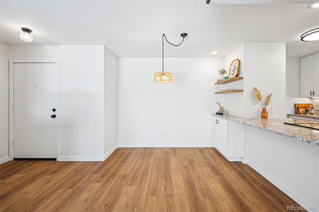 kitchen featuring white cabinetry, light stone countertops, light wood-type flooring, and pendant lighting