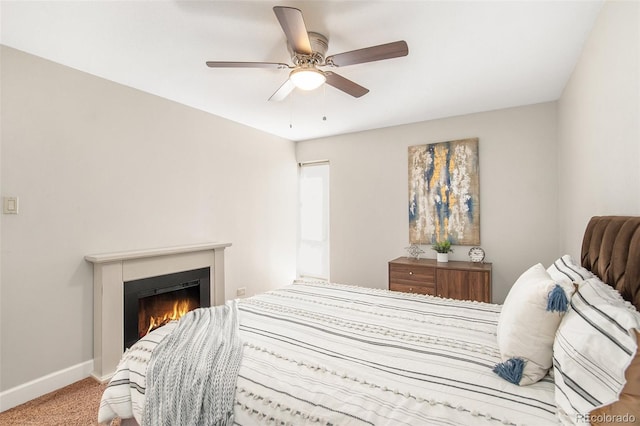 bedroom featuring a warm lit fireplace, a ceiling fan, baseboards, and carpet floors