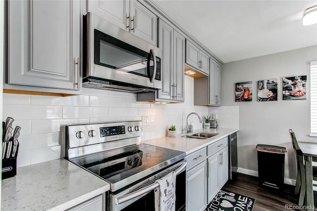 kitchen featuring sink, gray cabinetry, backsplash, stainless steel appliances, and light stone countertops