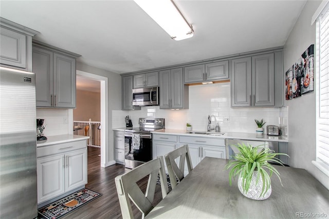 kitchen featuring sink, gray cabinetry, tasteful backsplash, appliances with stainless steel finishes, and dark hardwood / wood-style floors