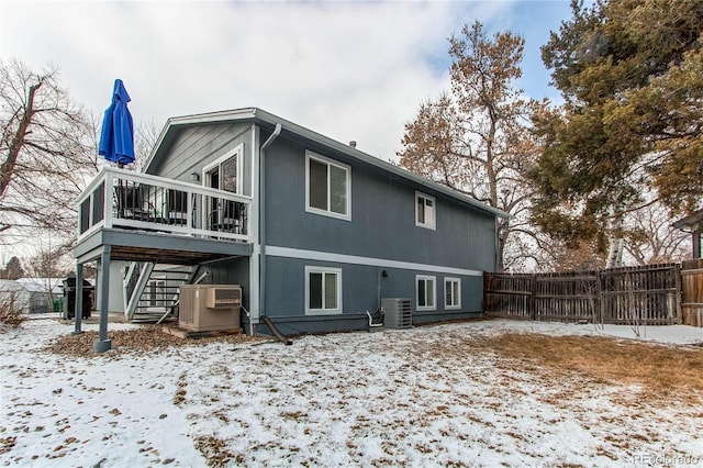 snow covered back of property with central AC and a deck