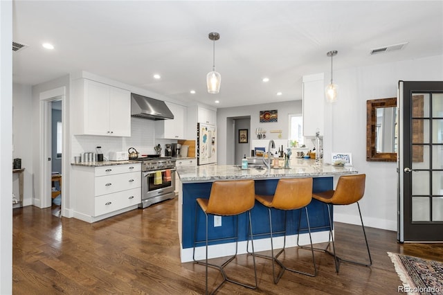 kitchen with white cabinets, white refrigerator, high end range, wall chimney range hood, and dark hardwood / wood-style flooring