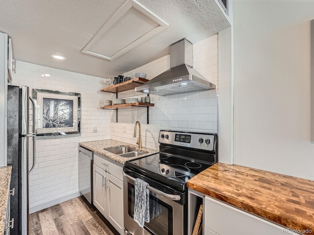 kitchen featuring wall chimney range hood, sink, hardwood / wood-style flooring, appliances with stainless steel finishes, and butcher block countertops