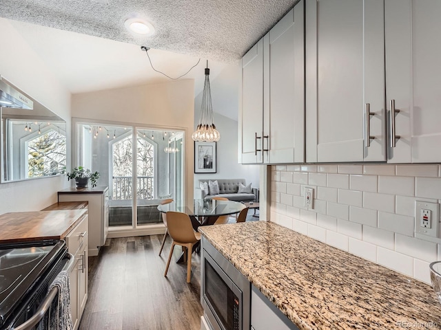 kitchen featuring light stone countertops, stove, backsplash, stainless steel microwave, and lofted ceiling