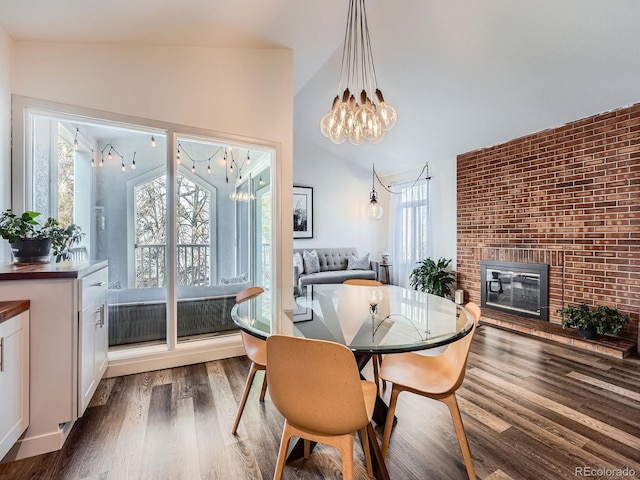 dining room featuring dark hardwood / wood-style floors, vaulted ceiling, and a brick fireplace