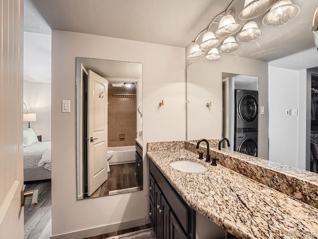 full bathroom featuring stacked washer / dryer, vanity, wood-type flooring, and a textured ceiling