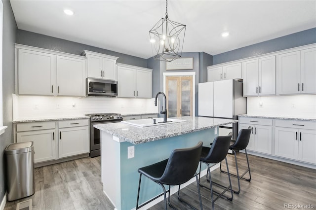 kitchen with a kitchen island with sink, wood finished floors, a sink, appliances with stainless steel finishes, and backsplash