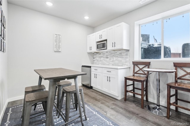 kitchen with stainless steel appliances, backsplash, white cabinets, wood finished floors, and baseboards