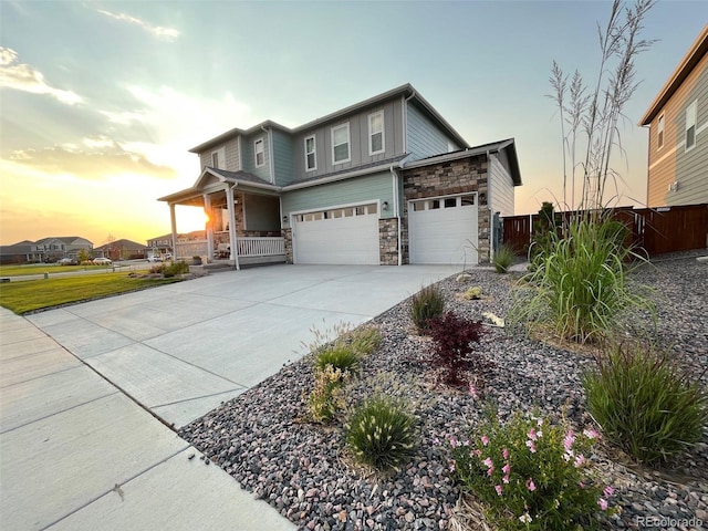 view of front facade featuring covered porch, concrete driveway, an attached garage, fence, and stone siding