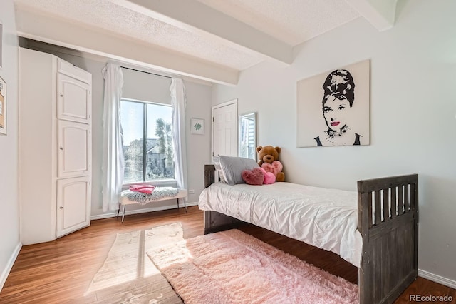 bedroom with a textured ceiling, wood finished floors, beam ceiling, and baseboards