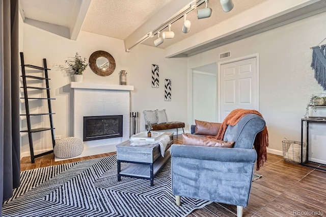 living area with baseboards, visible vents, a textured ceiling, a fireplace, and beam ceiling