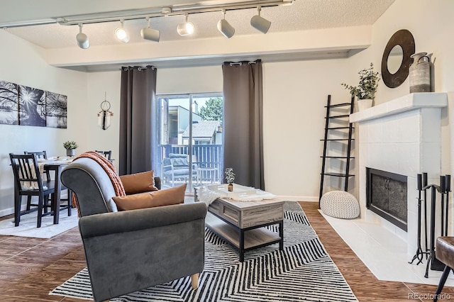 living area featuring a tile fireplace, dark wood finished floors, a textured ceiling, and baseboards