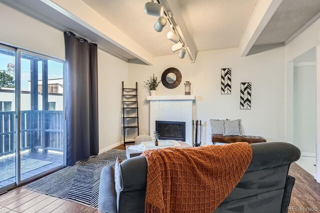 living room with a textured ceiling, a fireplace, wood finished floors, baseboards, and beam ceiling