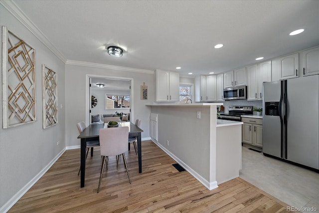 kitchen with light wood finished floors, crown molding, light countertops, stainless steel appliances, and white cabinetry