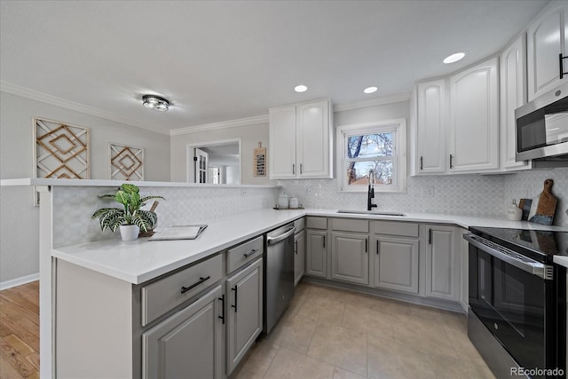 kitchen with a peninsula, ornamental molding, gray cabinetry, a sink, and appliances with stainless steel finishes