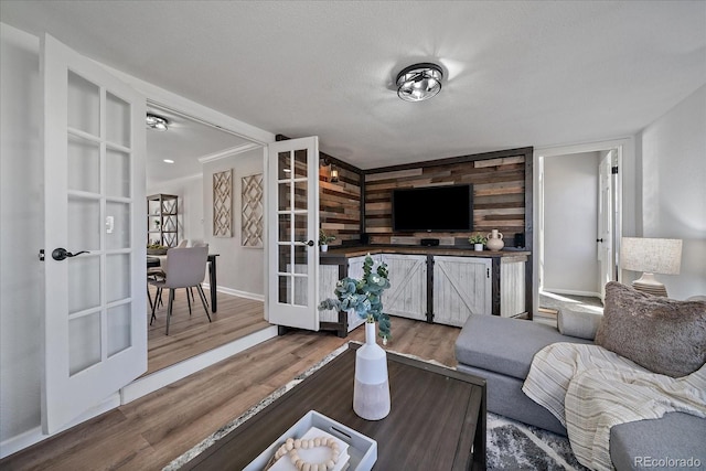 living room featuring a textured ceiling, wood finished floors, french doors, wooden walls, and baseboards