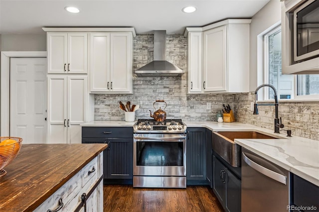 kitchen with wood counters, stainless steel appliances, white cabinets, and wall chimney exhaust hood