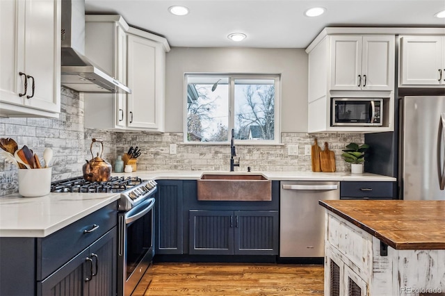 kitchen with blue cabinetry, stainless steel appliances, white cabinetry, and wall chimney exhaust hood