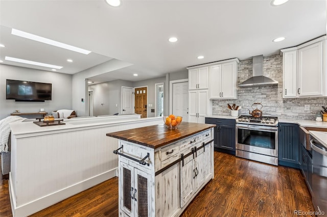 kitchen with wall chimney exhaust hood, stainless steel appliances, blue cabinetry, butcher block countertops, and white cabinetry