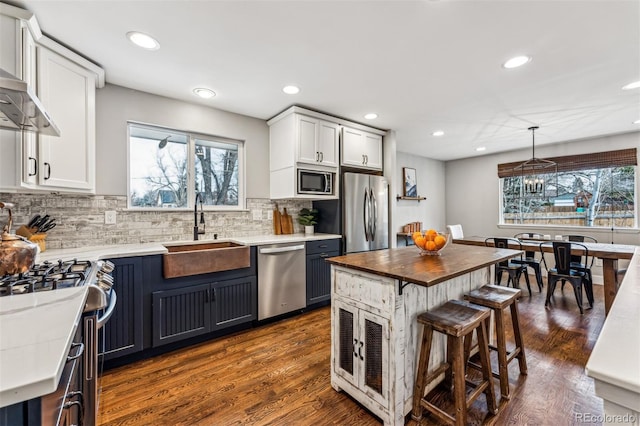 kitchen with a center island, sink, hanging light fixtures, white cabinetry, and stainless steel appliances