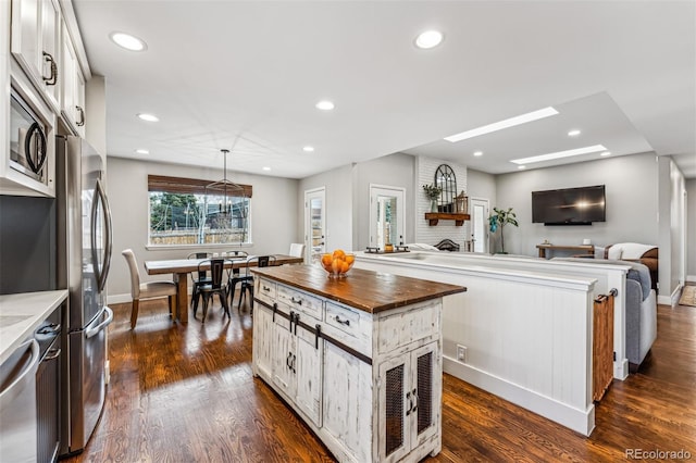 kitchen with white cabinets, a fireplace, butcher block countertops, decorative light fixtures, and a kitchen island