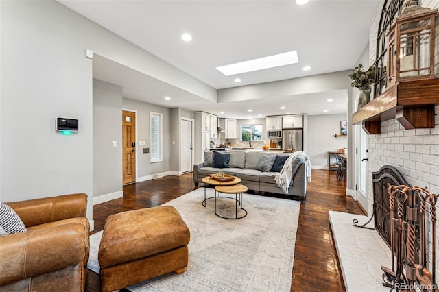 living room with a skylight, wood-type flooring, and a brick fireplace