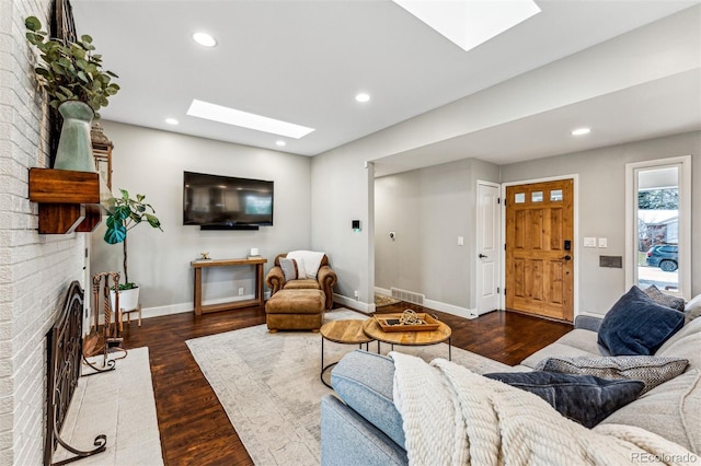 living room featuring a skylight, dark hardwood / wood-style flooring, and a brick fireplace