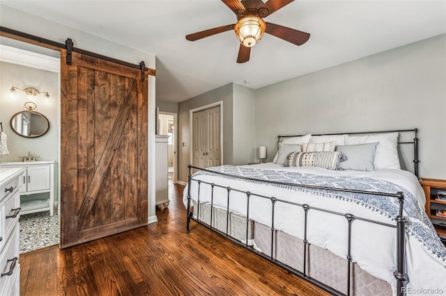 bedroom featuring ceiling fan, a barn door, dark hardwood / wood-style floors, ensuite bathroom, and a closet