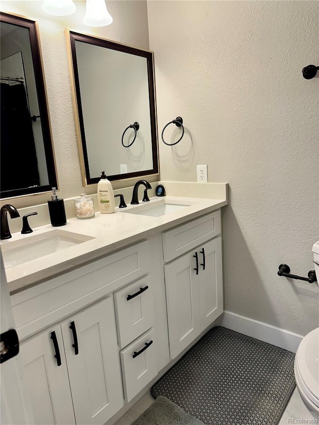 bathroom featuring double vanity, toilet, baseboards, and a sink