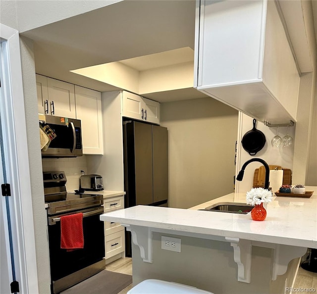 kitchen with light stone counters, a breakfast bar, a sink, stainless steel appliances, and white cabinetry