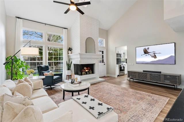 living area with a brick fireplace, high vaulted ceiling, a ceiling fan, and wood finished floors